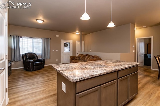 kitchen featuring decorative light fixtures, light stone countertops, a center island, and light hardwood / wood-style flooring