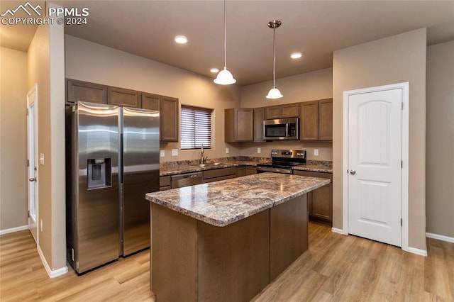 kitchen featuring light wood-type flooring, pendant lighting, stainless steel appliances, a center island, and sink