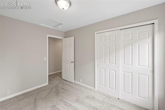 unfurnished bedroom with a closet, carpet, attic access, and baseboards