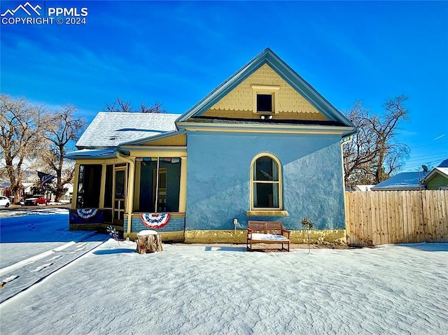 snow covered back of property with a sunroom, fence, and stucco siding