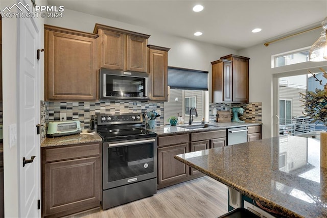 kitchen with tasteful backsplash, sink, dark stone counters, stainless steel appliances, and light hardwood / wood-style flooring