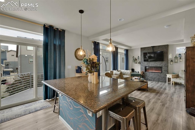 kitchen with pendant lighting, a fireplace, dark stone countertops, a kitchen bar, and light hardwood / wood-style floors