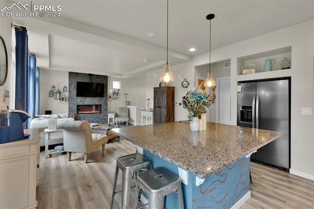 kitchen featuring decorative light fixtures, a breakfast bar area, a center island, light stone counters, and stainless steel fridge with ice dispenser