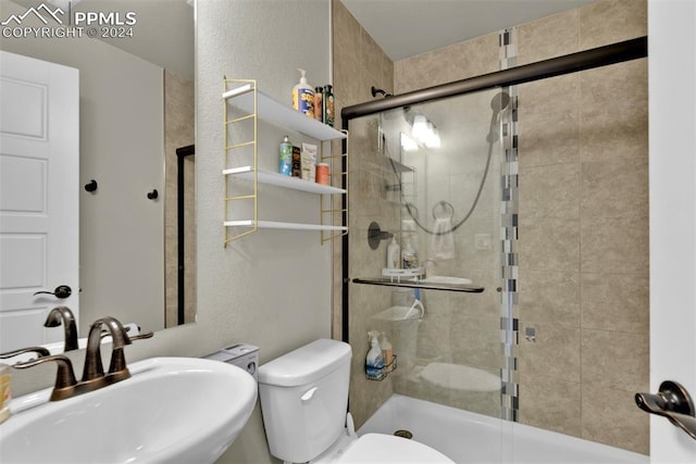 bathroom with toilet, a shower with door, and sink