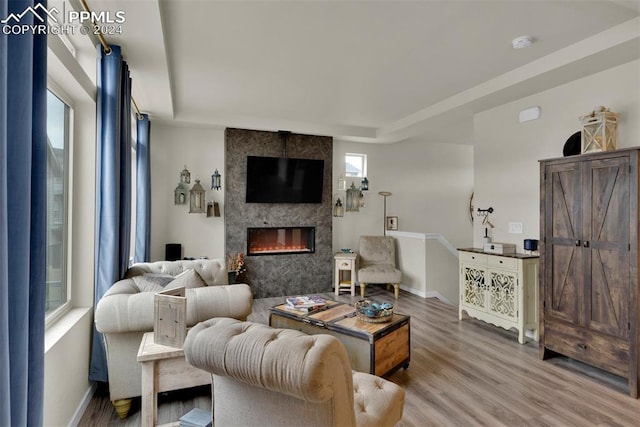 living room featuring a raised ceiling, hardwood / wood-style floors, and a tile fireplace