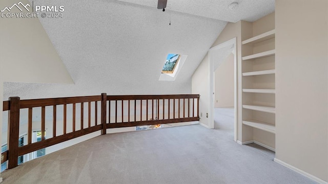 additional living space with lofted ceiling with skylight, a textured ceiling, built in shelves, ceiling fan, and light colored carpet