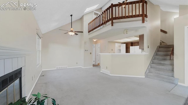 unfurnished living room with a fireplace, ceiling fan, high vaulted ceiling, a skylight, and carpet flooring