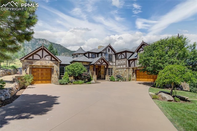 tudor house featuring a garage, stone siding, a mountain view, and concrete driveway