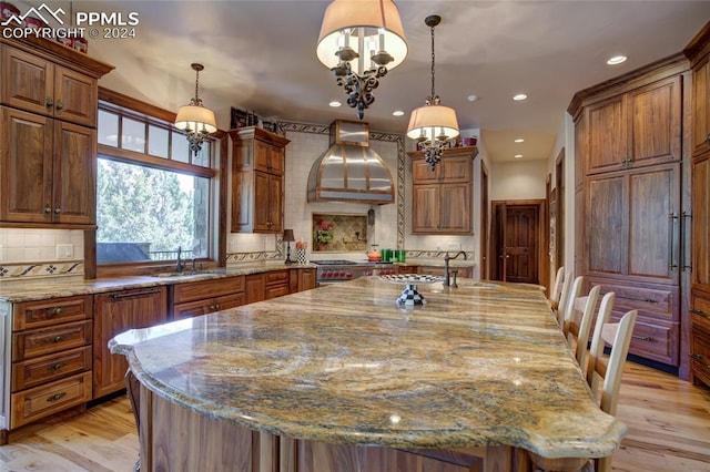 4950 Longwood Pt, Colorado Springs, CO 80906 - kitchen with light stone counters, brown cabinets, light wood-style flooring, a sink, and premium range hood