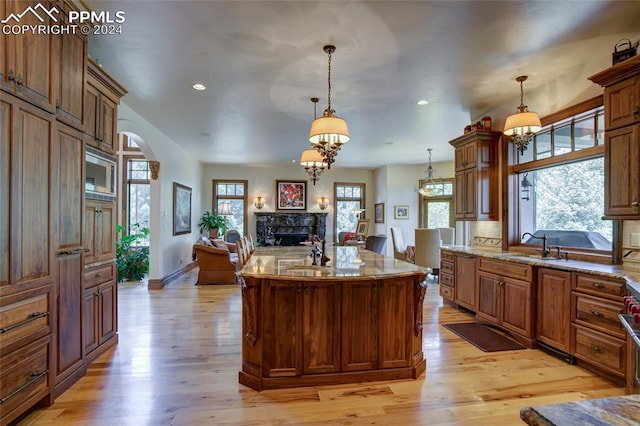 4950 Longwood Pt, Colorado Springs, CO 80906 - kitchen with arched walkways, light stone counters, a fireplace, a sink, and light wood-style floors