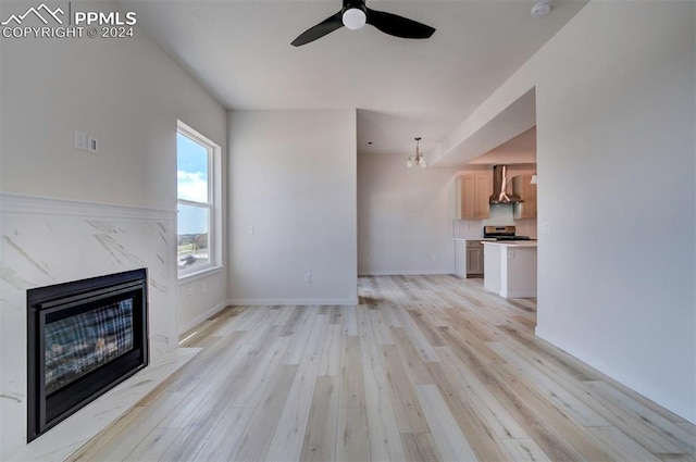 unfurnished living room featuring a fireplace, ceiling fan with notable chandelier, and light hardwood / wood-style flooring