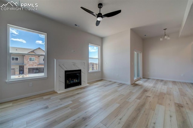 unfurnished living room featuring light hardwood / wood-style floors, ceiling fan with notable chandelier, and a fireplace