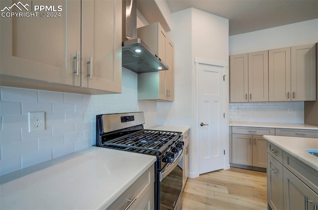 kitchen with gray cabinets, stainless steel gas range, decorative backsplash, light wood-type flooring, and range hood