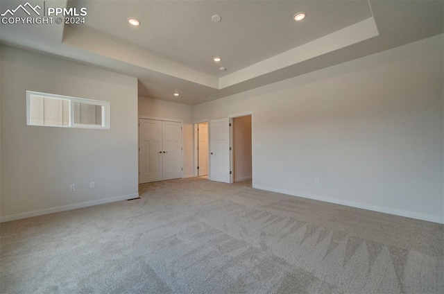 unfurnished bedroom with light colored carpet and a tray ceiling