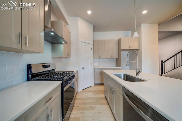 kitchen with wall chimney range hood, stainless steel appliances, tasteful backsplash, sink, and hanging light fixtures