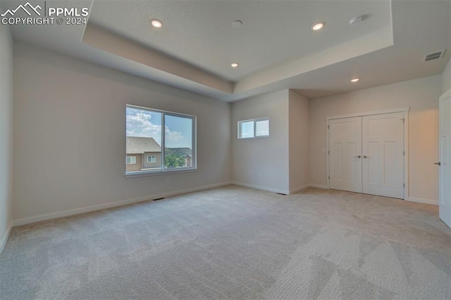 unfurnished bedroom featuring light carpet and a raised ceiling