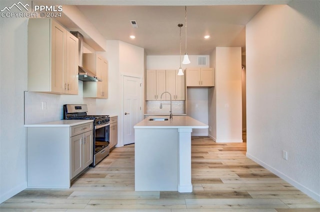 kitchen with an island with sink, stainless steel gas range, tasteful backsplash, hanging light fixtures, and sink