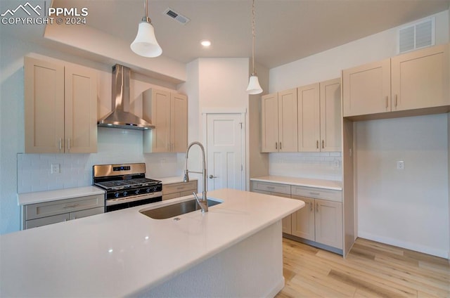 kitchen featuring hanging light fixtures, sink, wall chimney exhaust hood, and stainless steel gas range