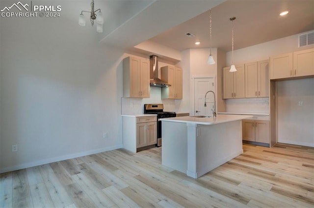 kitchen featuring a center island with sink, stainless steel gas range oven, pendant lighting, wall chimney exhaust hood, and sink