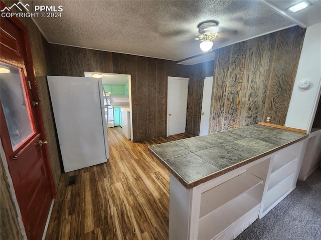 kitchen featuring ceiling fan, wooden walls, white appliances, light hardwood / wood-style floors, and a textured ceiling