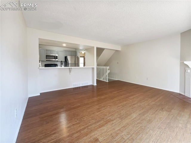 unfurnished living room with sink, a textured ceiling, and dark hardwood / wood-style flooring