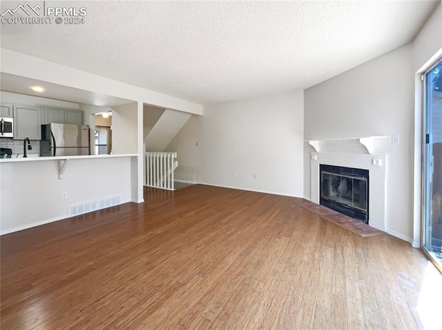 unfurnished living room featuring wood-type flooring, lofted ceiling, and a textured ceiling