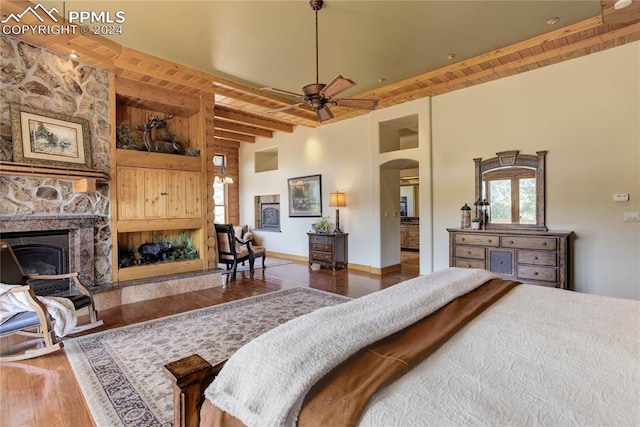 bedroom with arched walkways, a fireplace, wood finished floors, wooden ceiling, and beamed ceiling