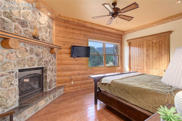 bedroom with ceiling fan, a fireplace, wood finished floors, and rustic walls