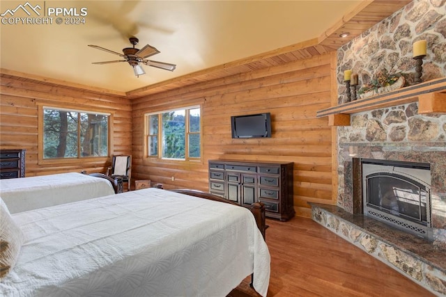 bedroom featuring ceiling fan, rustic walls, a fireplace, and wood finished floors