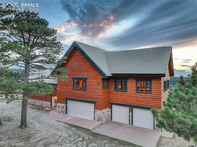 exterior space with an attached garage, stone siding, driveway, and faux log siding