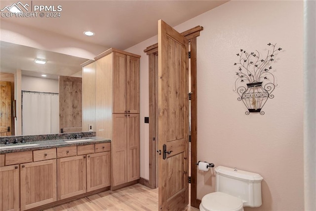 full bath with toilet, double vanity, a sink, and wood finished floors