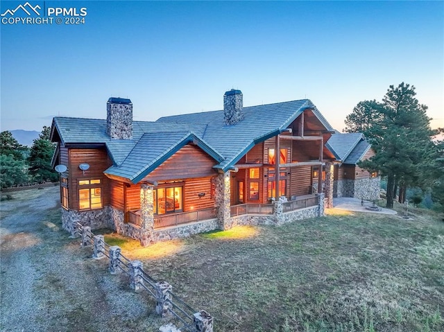 back of house with a yard, stone siding, a porch, and a chimney