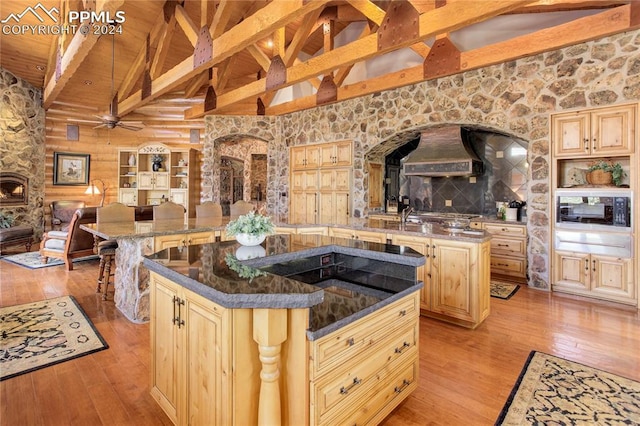 kitchen with light wood finished floors, a kitchen island, custom range hood, light brown cabinets, and black microwave