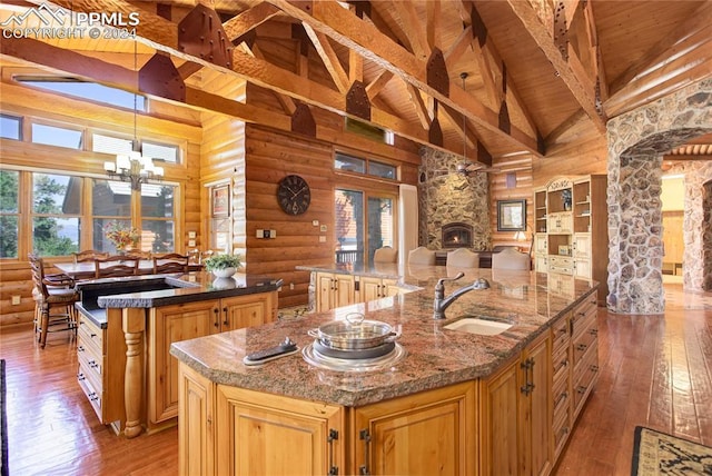 kitchen with a spacious island, a sink, a stone fireplace, light wood-type flooring, and beamed ceiling