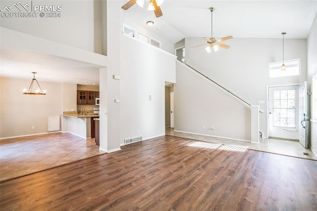 unfurnished living room with ceiling fan with notable chandelier, wood-type flooring, and high vaulted ceiling