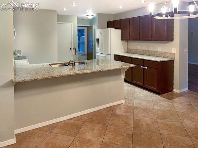 kitchen featuring sink, light stone countertops, white refrigerator with ice dispenser, and decorative light fixtures