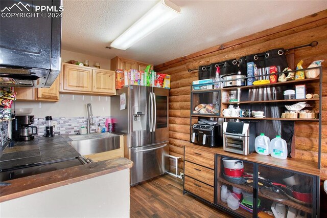 kitchen with light brown cabinetry, dark hardwood / wood-style flooring, stainless steel refrigerator, sink, and a textured ceiling