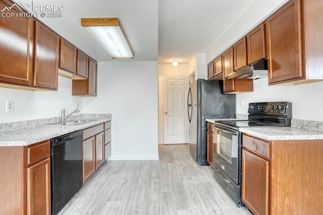 kitchen with light wood finished floors, light countertops, a sink, under cabinet range hood, and black appliances