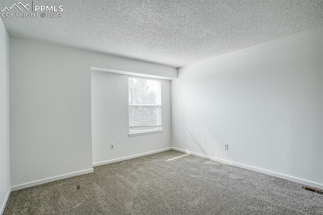 empty room featuring carpet floors, visible vents, a textured ceiling, and baseboards