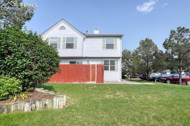 rear view of house featuring a lawn, a chimney, and fence