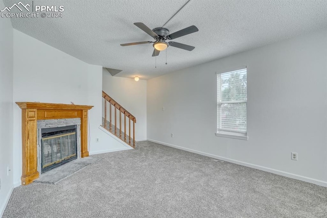 unfurnished living room with a textured ceiling, carpet floors, a fireplace with flush hearth, baseboards, and stairway