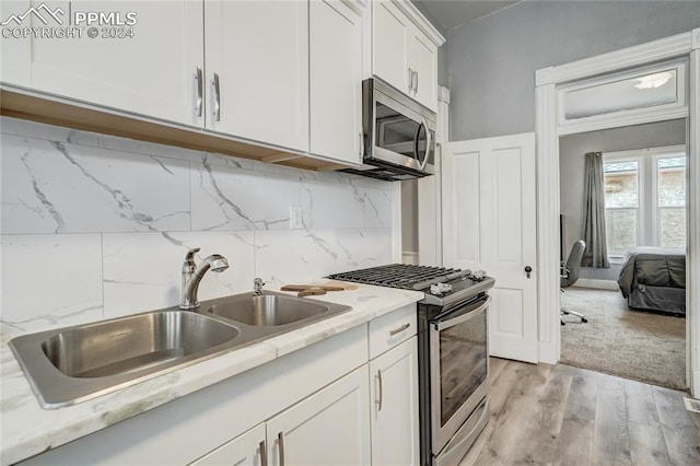 kitchen featuring appliances with stainless steel finishes, sink, backsplash, white cabinets, and light hardwood / wood-style floors