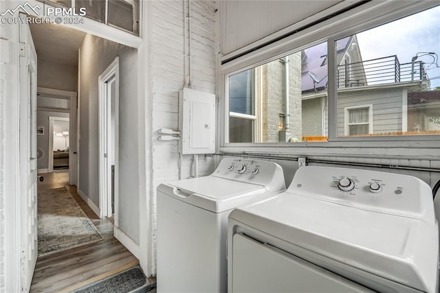 clothes washing area featuring wood-type flooring, separate washer and dryer, electric panel, and wooden walls