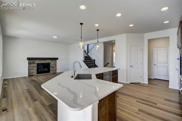 kitchen featuring dark wood-type flooring, sink, a fireplace, hanging light fixtures, and an island with sink