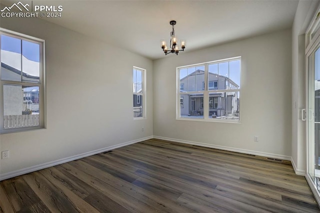 empty room with dark hardwood / wood-style flooring and an inviting chandelier