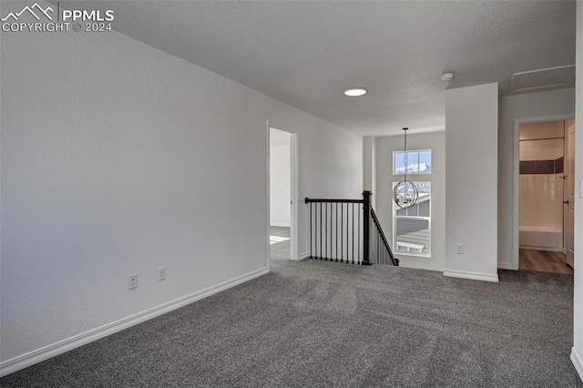 unfurnished room featuring baseboards, a textured ceiling, a chandelier, and dark carpet