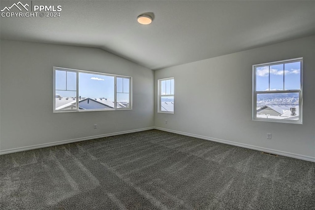 spare room with vaulted ceiling, visible vents, dark colored carpet, and baseboards