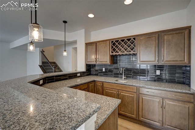 kitchen with stone counters, hanging light fixtures, backsplash, and a sink