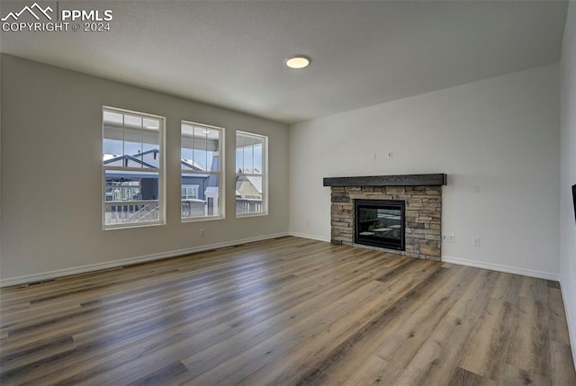 unfurnished living room with a stone fireplace, a textured ceiling, baseboards, and wood finished floors