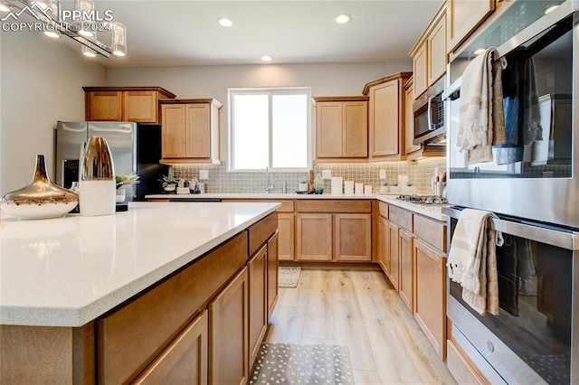 kitchen with light wood-style flooring, a kitchen island, appliances with stainless steel finishes, and decorative backsplash